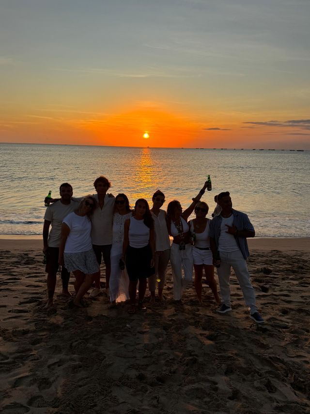 Un gruppo WeRoad posa su una spiaggia sabbiosa, stagliato contro un vibrante tramonto arancione sul mare.