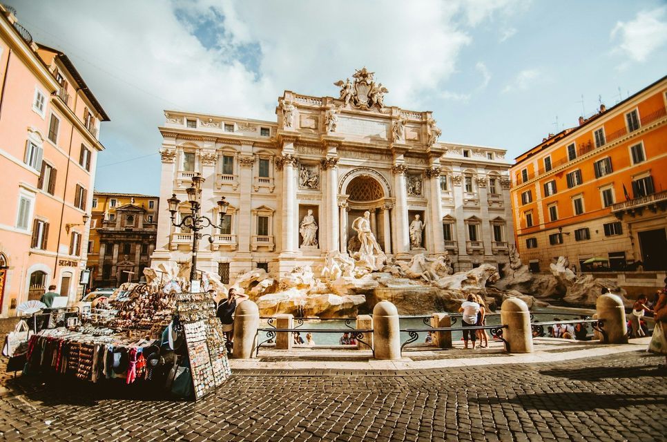 Une fontaine en marbre blanc ornée sur une place de ville par une journée ensoleillée, avec un stand de souvenirs au premier plan pavé.