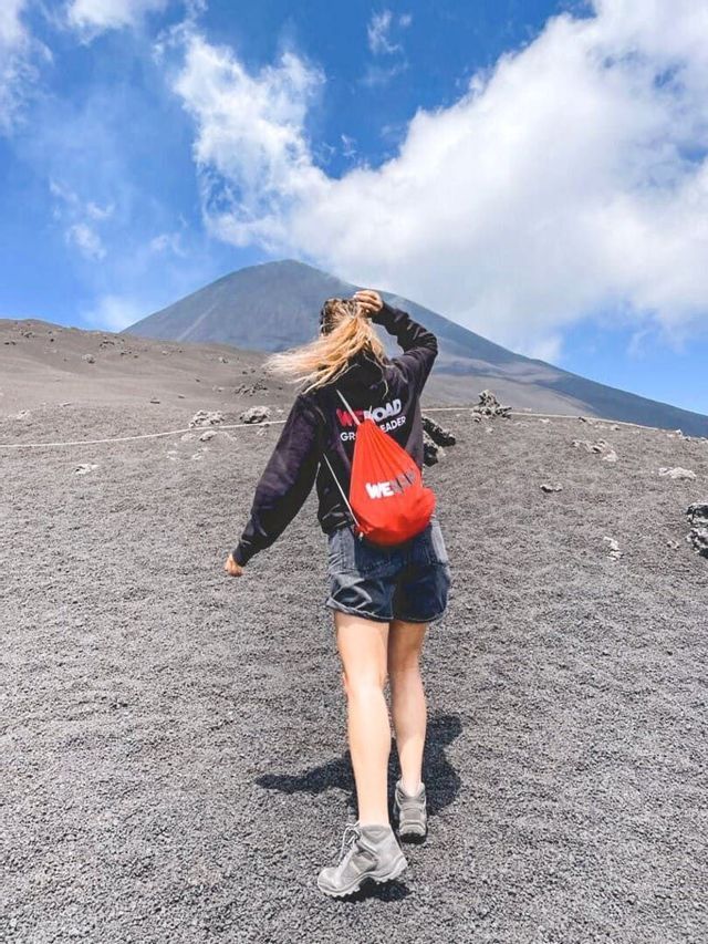 Un líder de grupo WeRoad, de espaldas, subiendo por una ladera volcánica de grava hacia la cima.