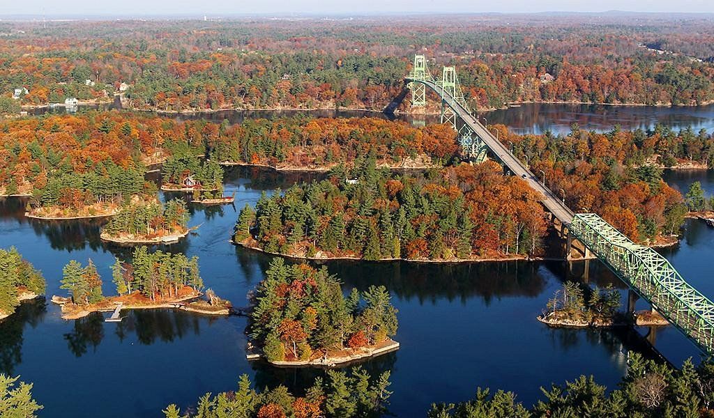 Una vista aerea di un grande ponte verde che attraversa uno specchio d'acqua con molte piccole isole coperte di fogliame autunnale.