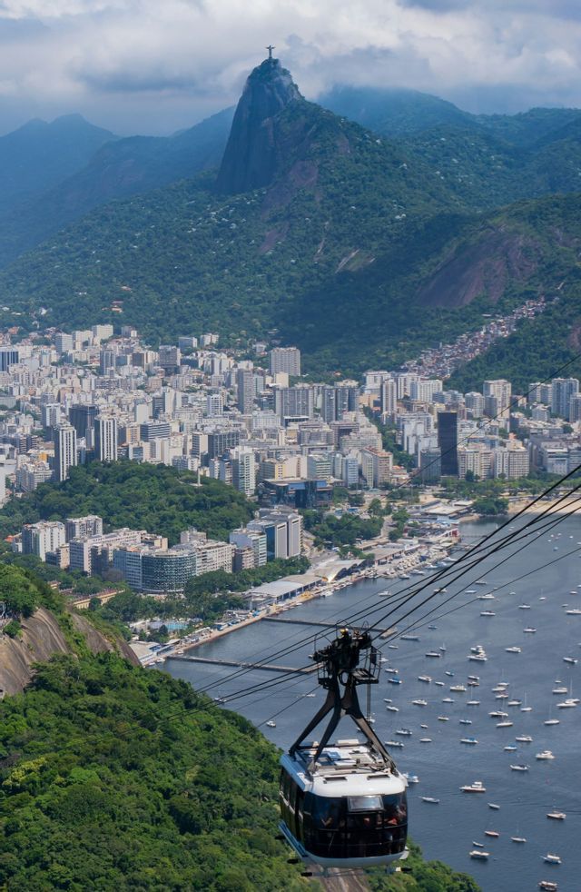 Una funivia viaggia sopra una baia piena di barche, con una città costiera e montagne verdi sullo sfondo.