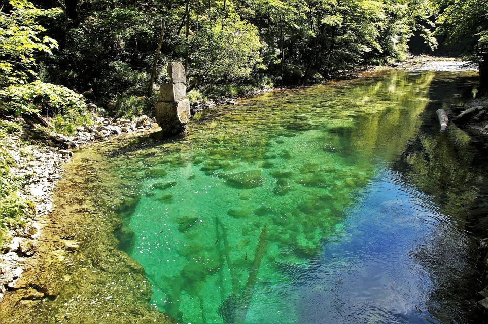 Un fiume limpido e turchese scorre attraverso una foresta lussureggiante e verde, con un pilastro di pietra che si erge sulla riva rocciosa.