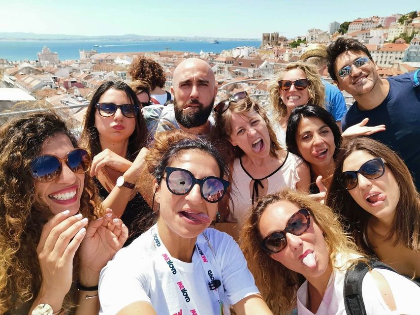 Un grupo de WeRoad se toma una selfie divertida, sacando la lengua en un día soleado, con vistas a una ciudad y al mar.
