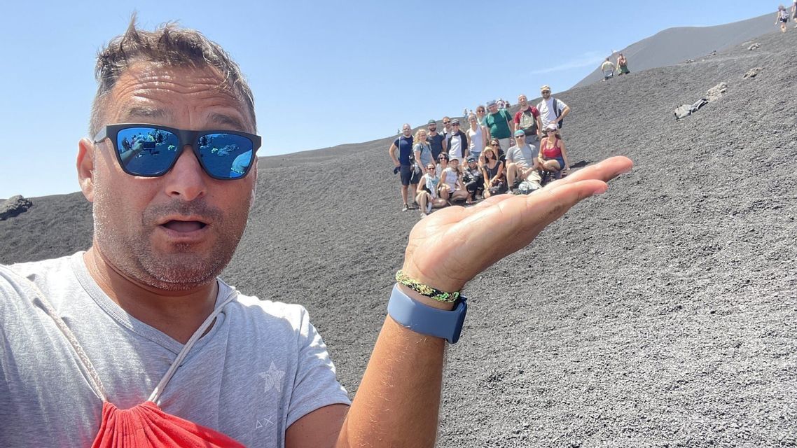 Un selfie en gros plan d'un homme à la paume ouverte, créant une illusion de perspective forcée où il semble tenir un voyage de groupe WeRoad sur une colline sombre.