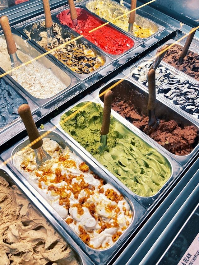 Une variété de parfums de gelato colorés disposés dans des bacs en métal à l'intérieur d'une vitrine, chacun avec une cuillère de service.