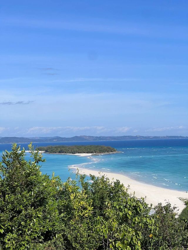 Una vista dall'alto su un fogliame verde che mostra una lingua di sabbia bianca che conduce a un'isola tropicale lussureggiante circondata da acqua turchese.