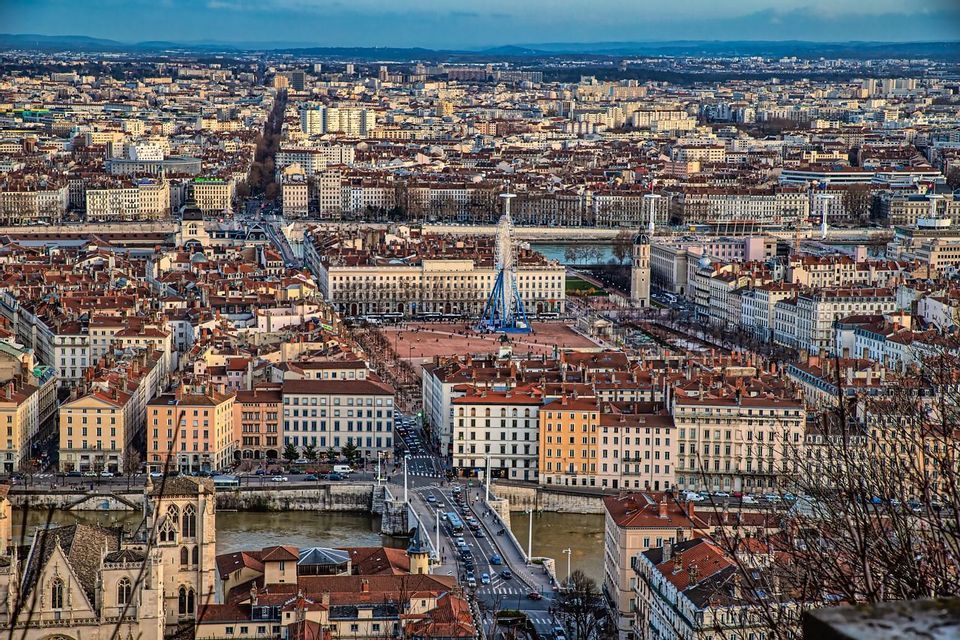 Un vasto paesaggio urbano visto dall'alto, con un fiume, un ponte e un'ampia piazza centrale con una ruota panoramica.
