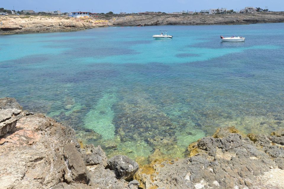 Due barche bianche ancorate in una baia tranquilla con acqua cristallina turchese e una costa rocciosa sullo sfondo.