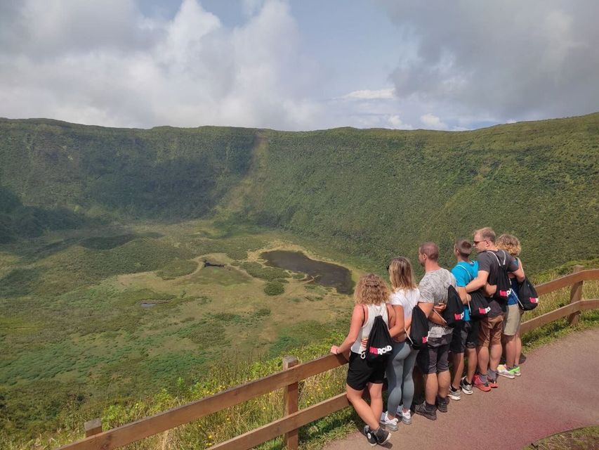 Un groupe WeRoad se tient à un point de vue, derrière une clôture en bois, et admire un grand cratère volcanique vert avec un lac.