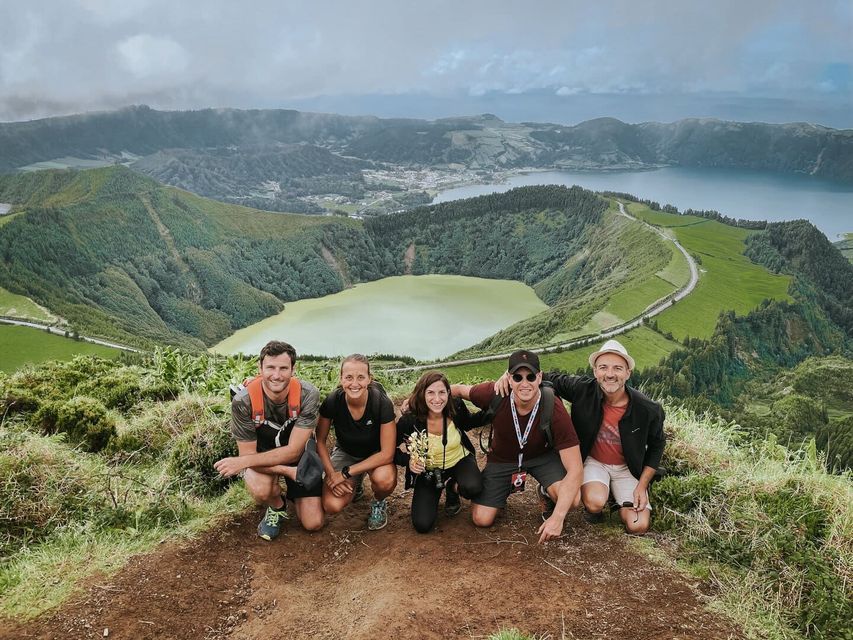Cinco personas de un grupo WeRoad agachadas en la cima de una colina, con vistas a un valle con dos lagos y colinas verdes.