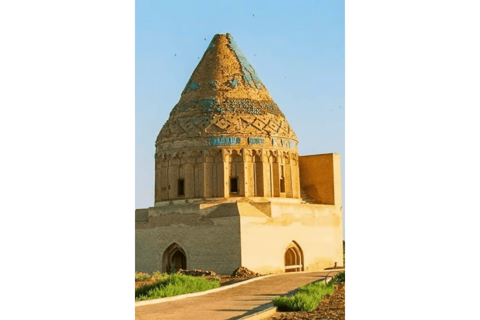 Mausoleo storico in pietra color sabbia con cupola conica, dettagli in piastrelle blu e intricato lavoro in mattoni.