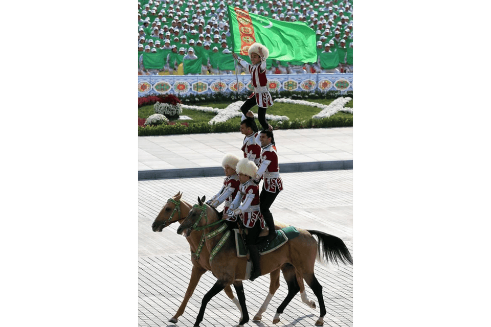 Un bambino sventola la bandiera del Turkmenistan dalla cima di una piramide umana formata da artisti equestri in abiti tradizionali.