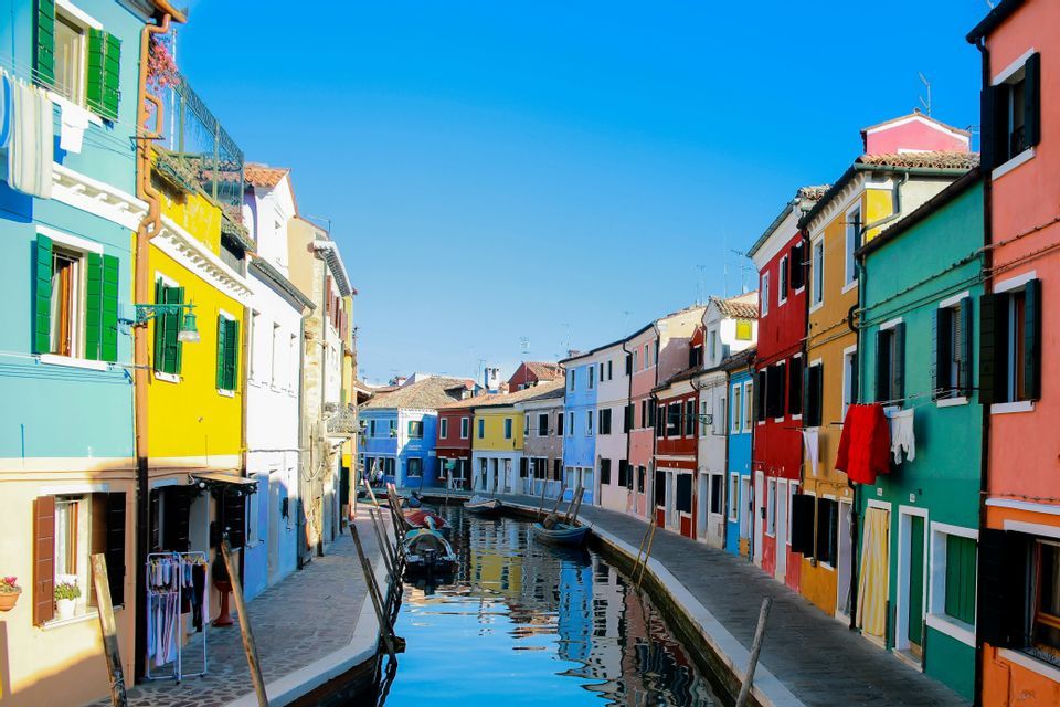 Brightly colored houses line a narrow water canal with several moored boats under a clear blue sky.