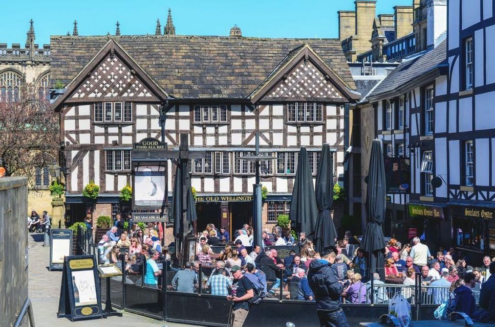 Una folla di persone sedute ai tavoli all'aperto e che socializzano davanti a un tradizionale pub in stile Tudor in una giornata di sole.