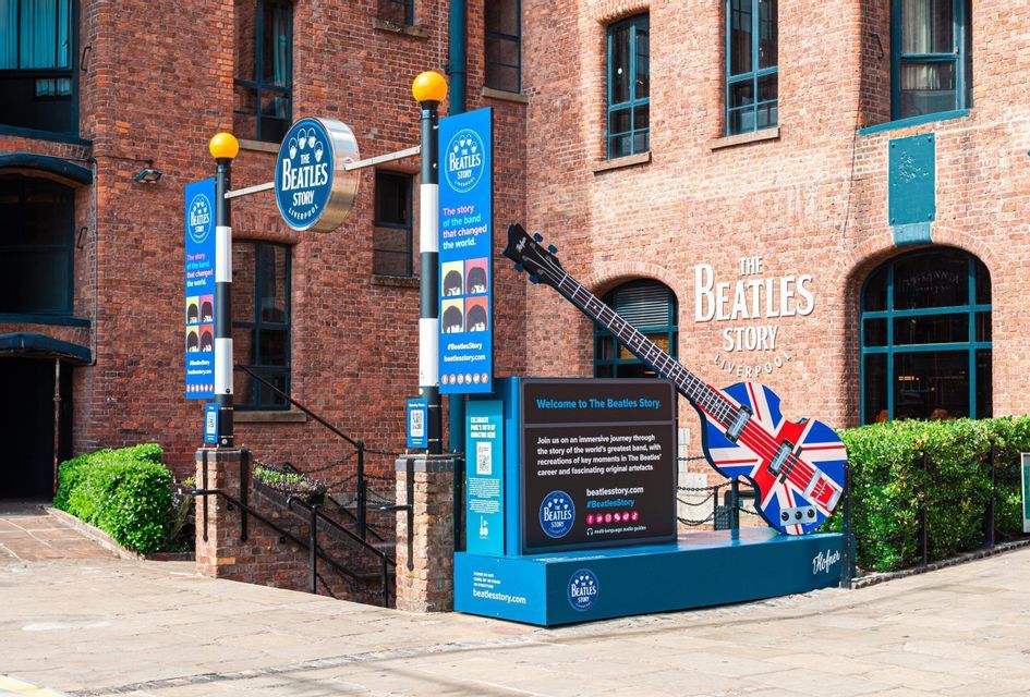 Una grande scultura di chitarra con design Union Jack all'ingresso del museo The Beatles Story, davanti a un edificio in mattoni.