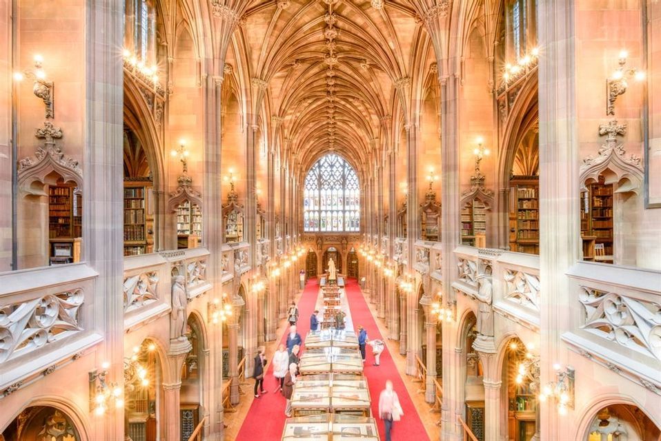 Vista dall'alto di persone che percorrono un tappeto rosso in una magnifica biblioteca storica con alti soffitti a volta e ricca architettura in pietra.