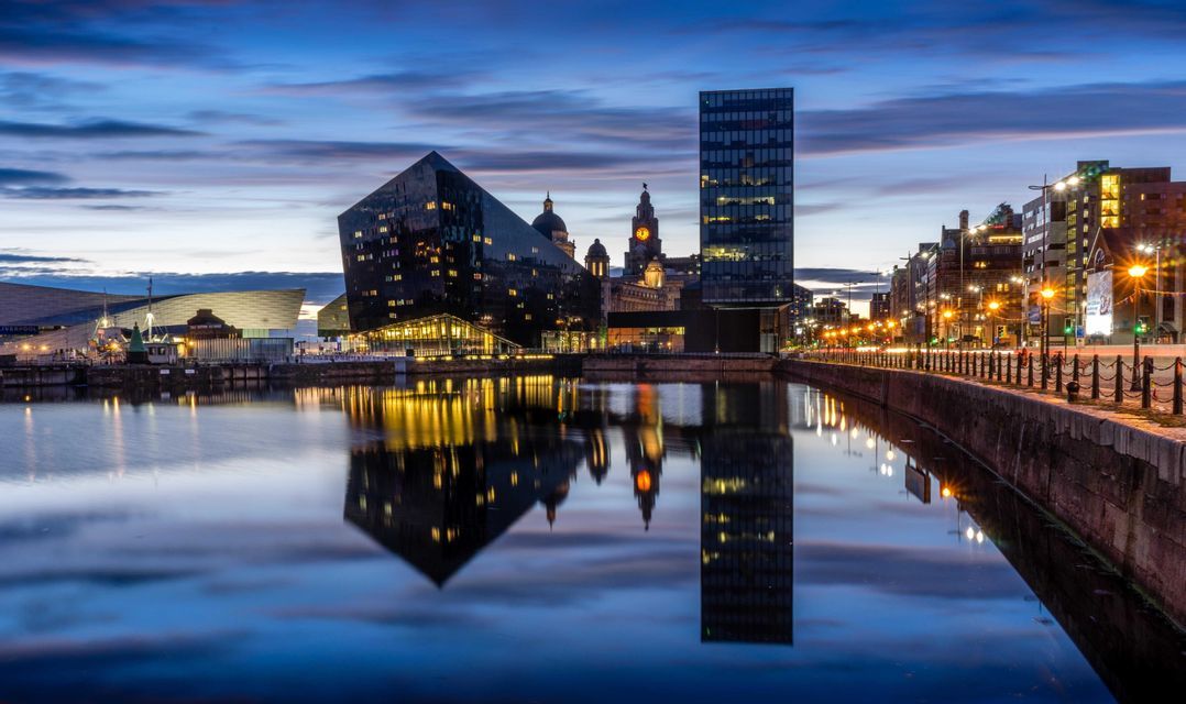 Uno skyline moderno con edifici illuminati che si riflettono nell'acqua calma di un porto al tramonto.