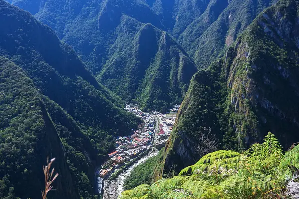 Vista a gran altura de un pueblo enclavado en un valle profundo, rodeado de montañas empinadas cubiertas de denso bosque verde.