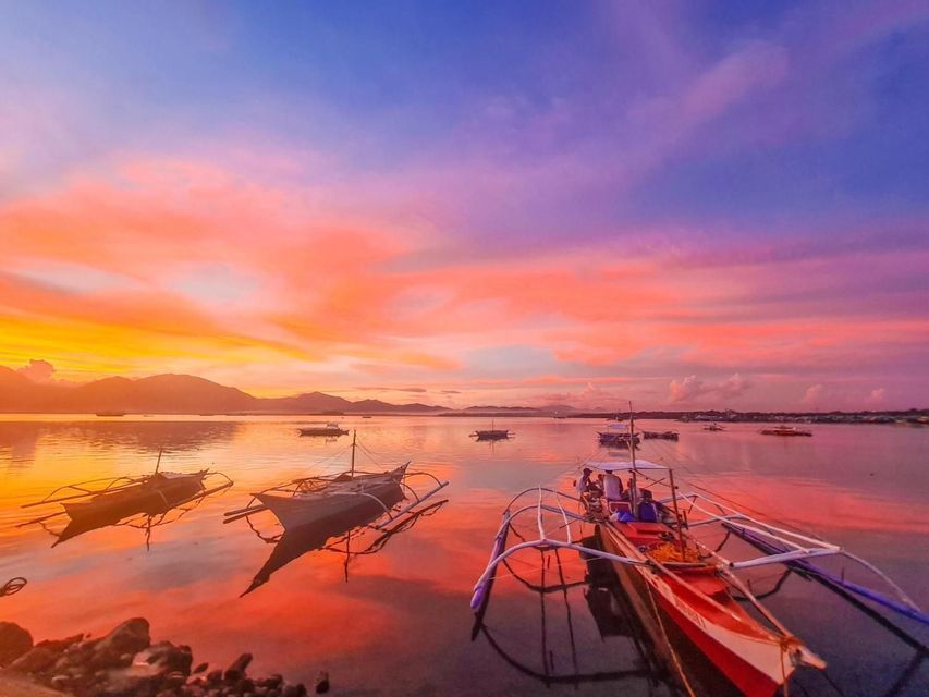 Barche a bilanciere galleggiano su acque calme sotto un tramonto vibrante arancione e viola, con montagne in lontananza.