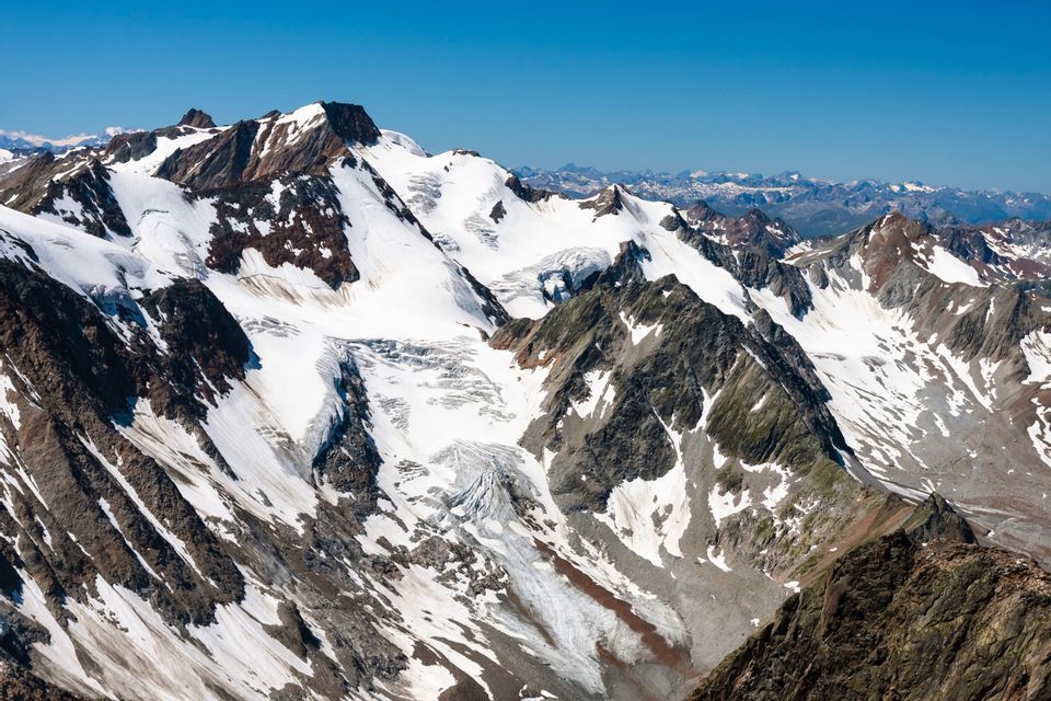 Ein zerklüftetes Gebirge mit Gletschern und schneebedeckten Gipfeln unter wolkenlosem blauem Himmel.