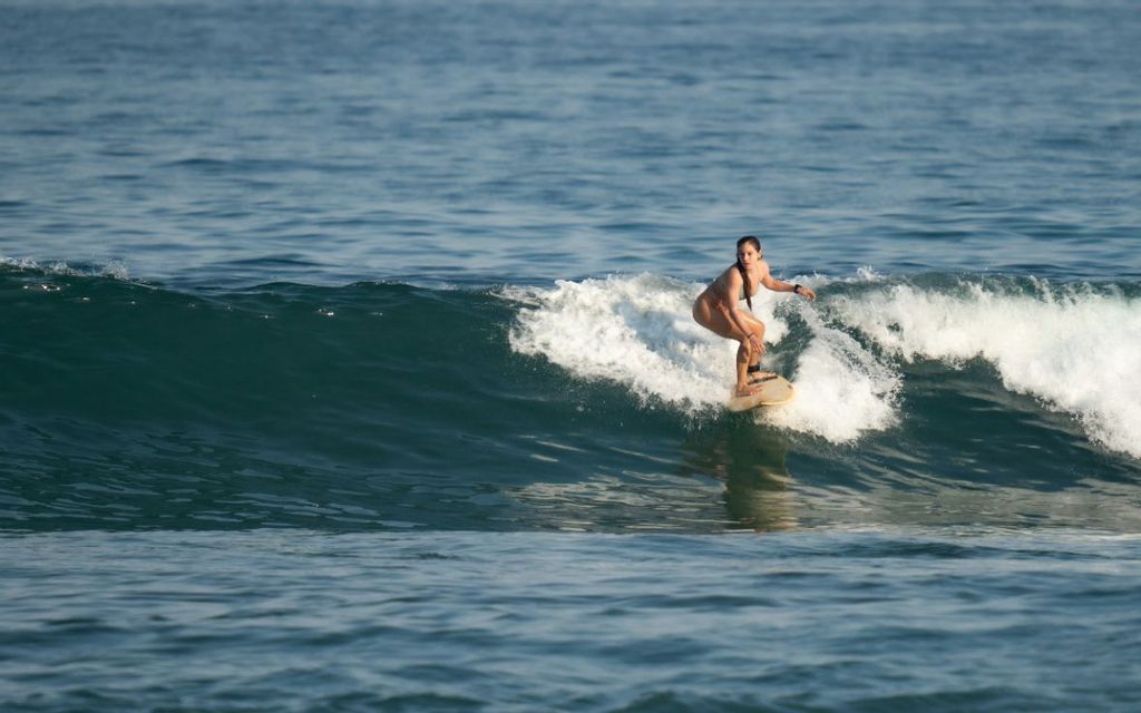 Una donna in bikini in equilibrio su una tavola da surf, cavalca un'onda nell'oceano aperto di giorno.