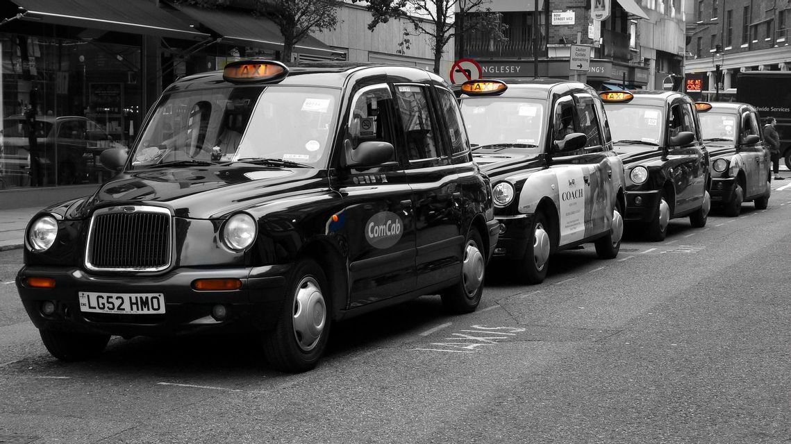 Una fila de taxis negros de Londres estacionados en una calle de la ciudad, con sus letreros amarillos resaltados en una foto en blanco y negro.