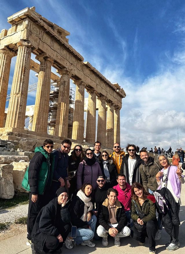 A WeRoad group trip posing for a photo in front of a large classical temple with stone columns under a blue sky.