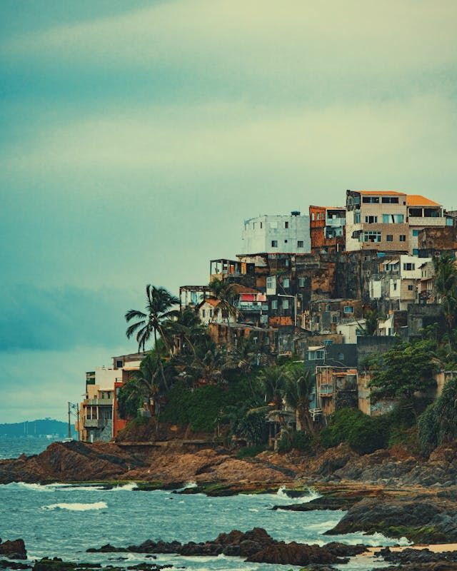 Un pueblo de edificios coloridos se asienta en una ladera rocosa y costera con palmeras y las olas del mar abajo.