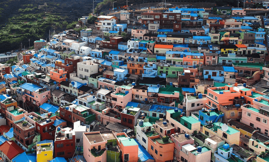 Case colorate con tetti blu brillanti sono addossate strettamente su un ripido versante verde in un villaggio denso.