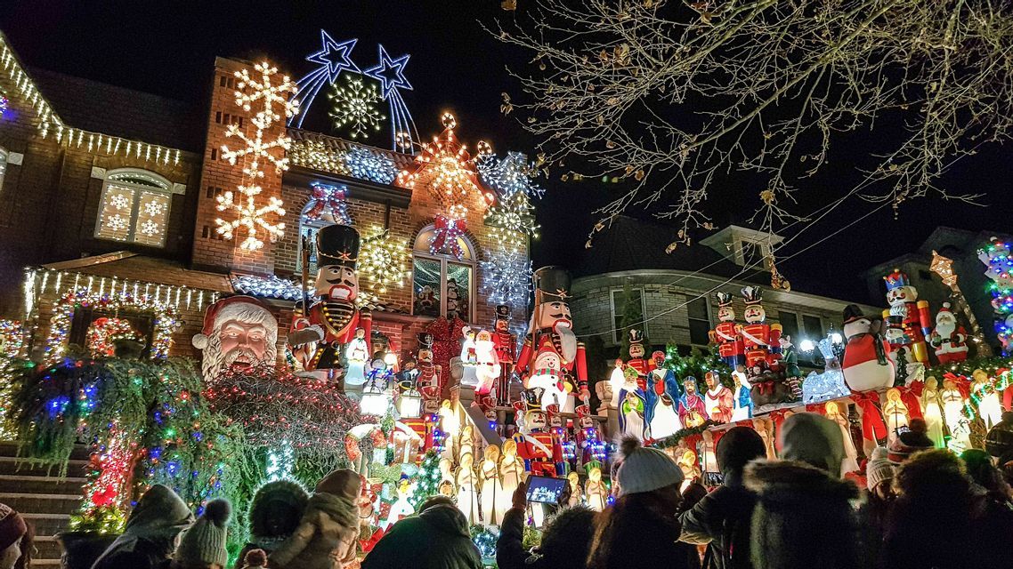 Eine Menschenmenge versammelt sich nachts, um ein aufwendig mit Weihnachtslichtern, Nussknackern und Weihnachtsmannfiguren geschmücktes Haus zu besichtigen.