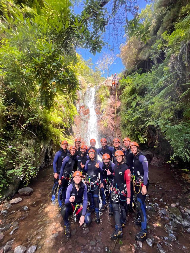 Un gruppo WeRoad in viaggio, con attrezzatura completa da canyoning, in posa in un torrente roccioso alla base di una cascata.