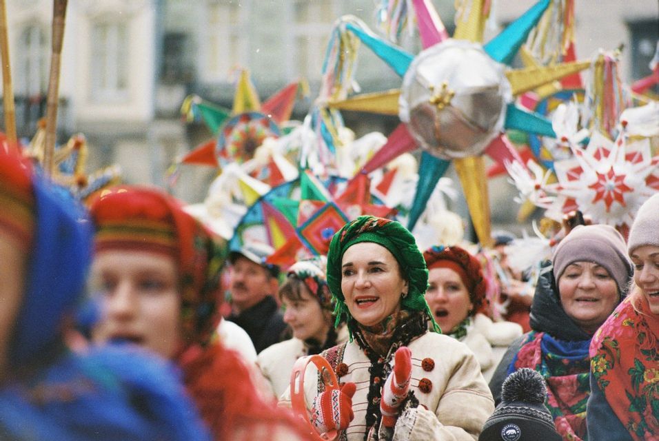 Eine Menschenmenge in farbenfroher Tracht nimmt an einer Straßenparade teil und hält große, dekorative Sterne.