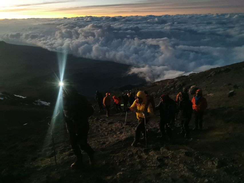 Un viaggio di gruppo WeRoad in trekking su un sentiero di montagna roccioso con lampade frontali all'alba, in alto sopra un mare di nuvole.