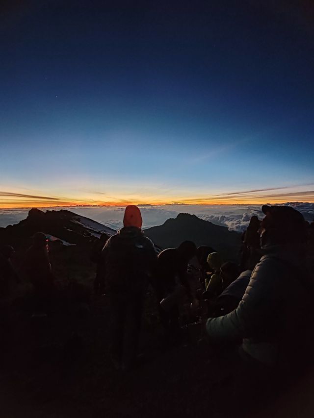 Un viaggio di gruppo WeRoad osserva l'alba da una cima di montagna, ammirando un mare di nuvole e vette lontane.
