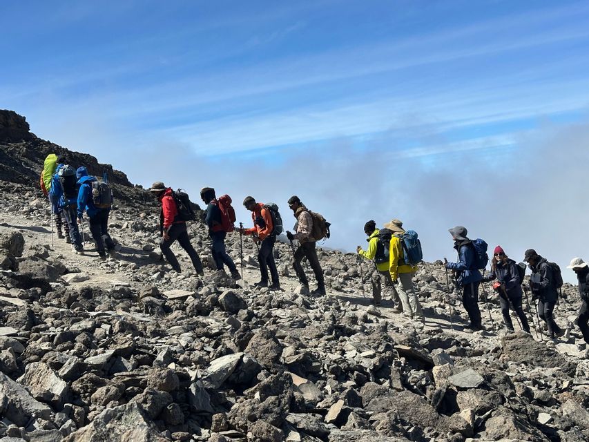 Un'escursione di gruppo WeRoad in fila indiana su un ripido sentiero di montagna roccioso sopra le nuvole.