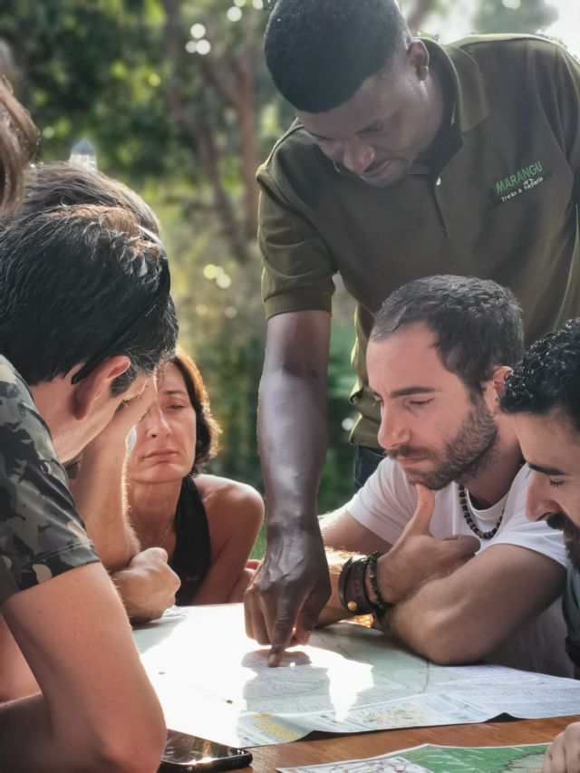 Una guida turistica indica un luogo su una mappa per un viaggio di gruppo WeRoad di viaggiatori riuniti attorno a un tavolo di legno all'aperto.