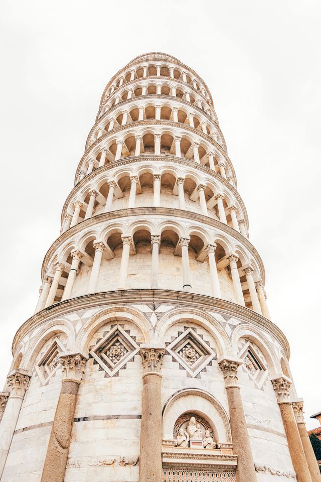 A low-angle view looking up at the ornate, circular tiers of a white marble tower with many arches and columns against a bright sky.
