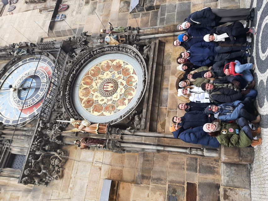Un groupe WeRoad prend la pose devant une grande horloge astronomique ornée sur un bâtiment en pierre.