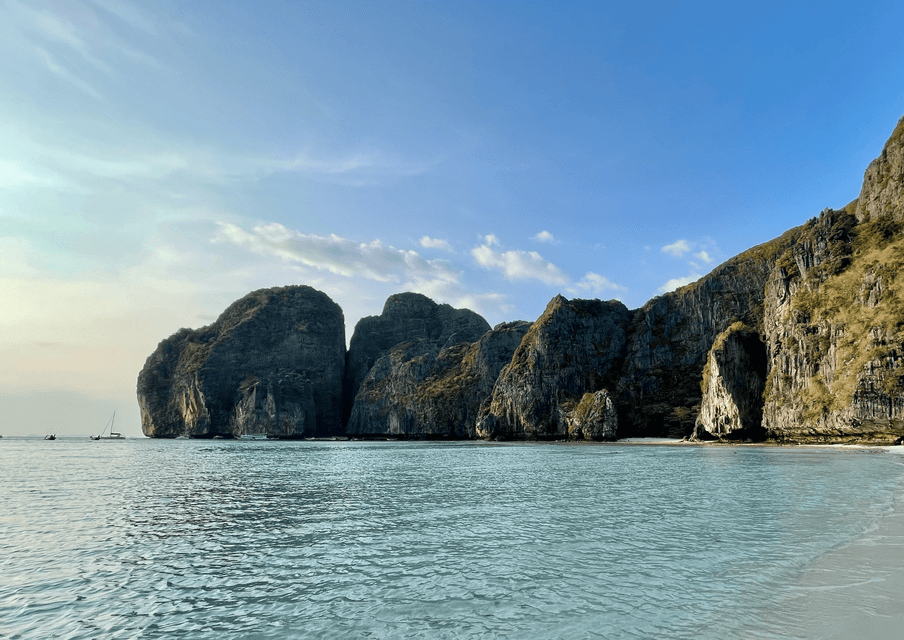 Grandi scogliere rocciose coperte di vegetazione emergono dalle acque calme e turchesi di una baia sotto un cielo azzurro e limpido.