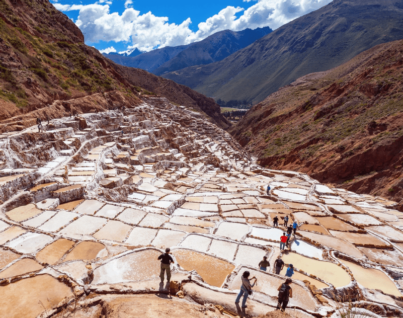 A WeRoad group trip walks among terraced salt pans built into a mountain valley under a bright blue sky.