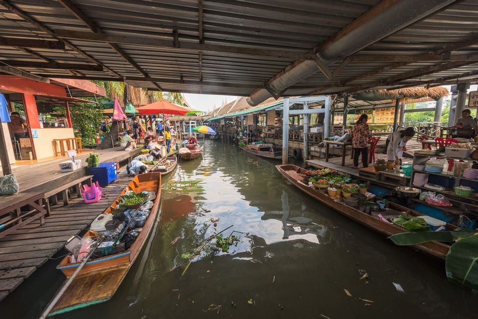 De longs bateaux en bois avec des vendeurs et des produits flottent sur un canal dans un marché couvert animé.