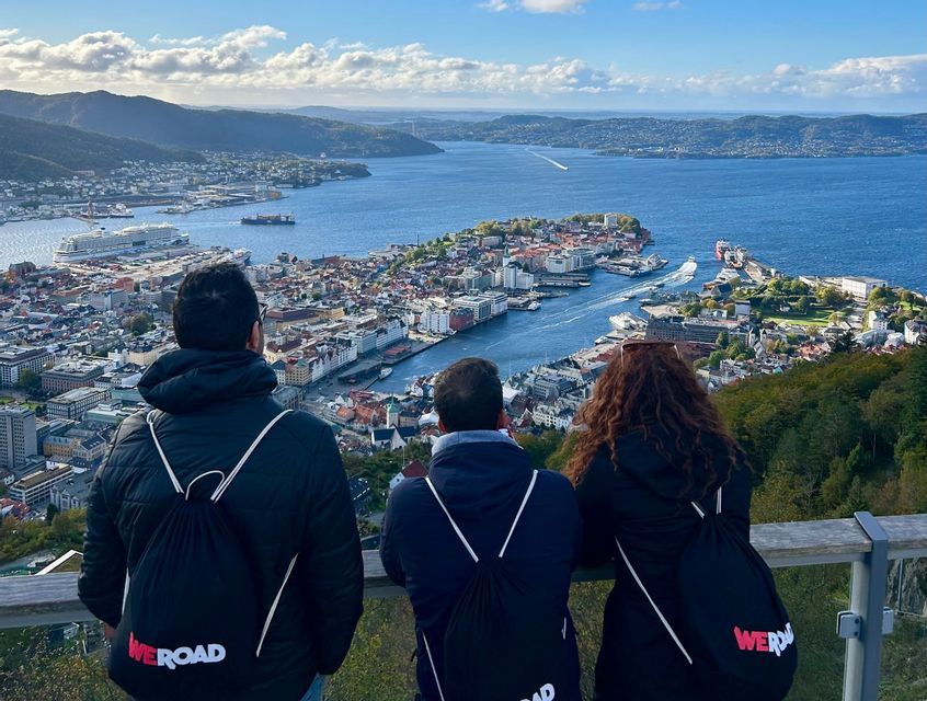 Un viaggio di gruppo WeRoad di tre persone viste di spalle, che osservano una città costiera e un porto da un punto panoramico.