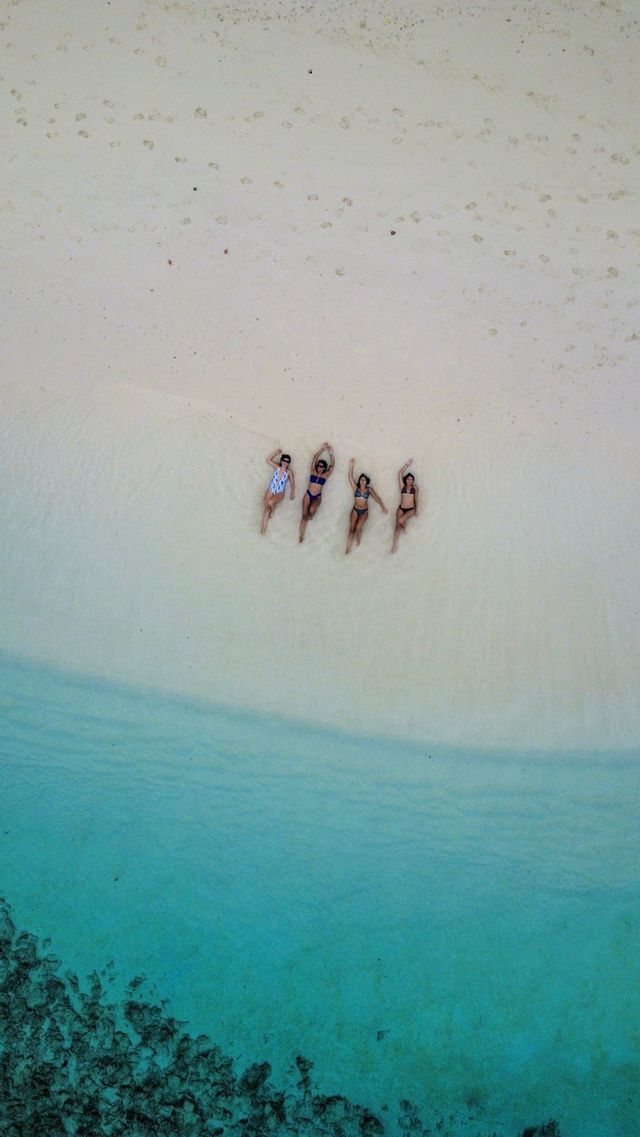 Una vista aérea de cuatro mujeres de un viaje en grupo de WeRoad tumbadas en las aguas poco profundas de color turquesa de una playa de arena blanca.