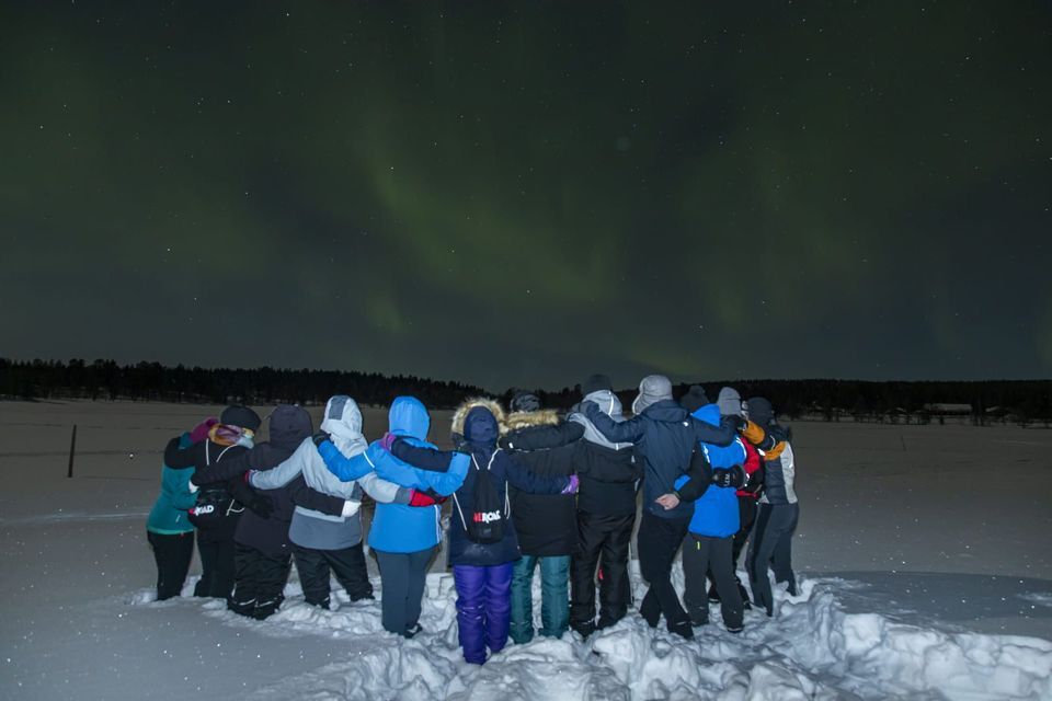 A WeRoad group trip with arms around each other, standing in the snow and watching the northern lights at night.