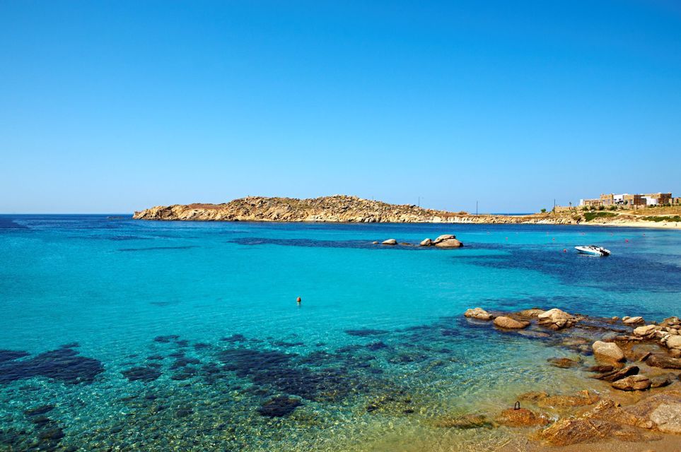 Una baia costiera con acqua cristallina turchese, una costa rocciosa e una piccola barca che galleggia sotto un cielo blu.