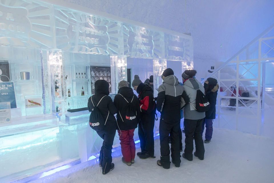 A WeRoad group trip wearing winter jackets stands at a bar counter inside a bar made entirely of ice.