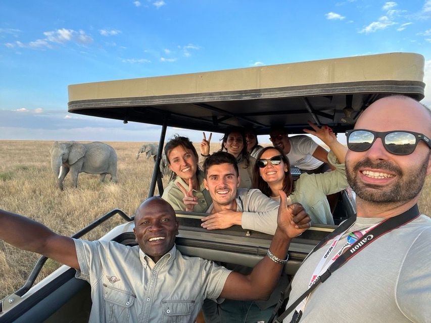 Un gruppo WeRoad in viaggio: persone sorridenti si scattano un selfie in un veicolo safari con elefanti sullo sfondo nella savana.