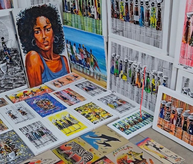 Una collezione di dipinti colorati raffiguranti figure africane, ritratti e fauna selvatica, disposti per esposizione e vendita.