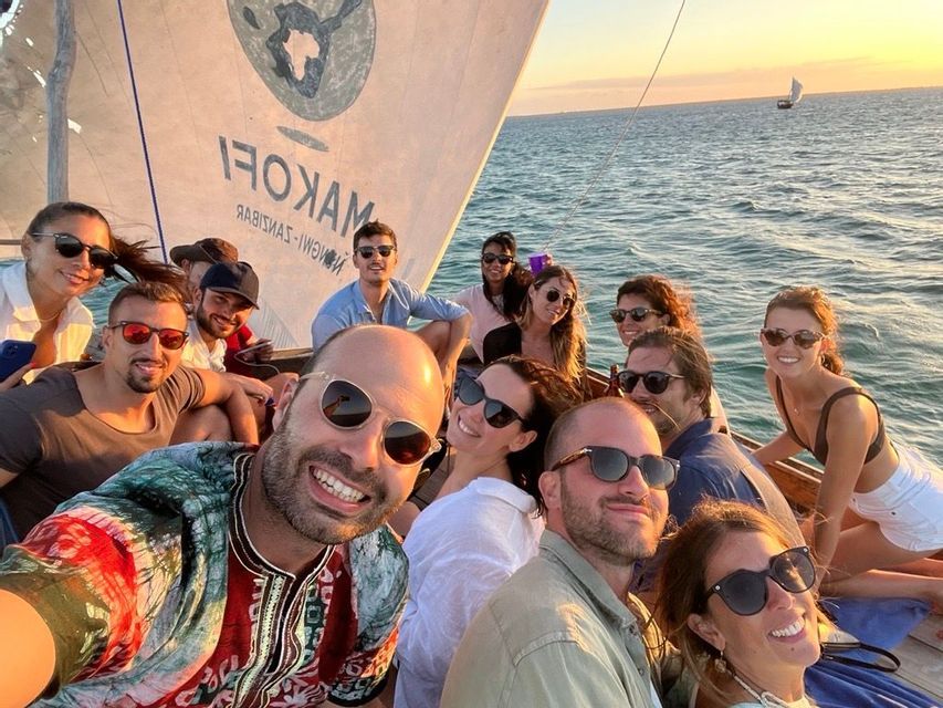 Un viaggio di gruppo WeRoad scatta un selfie sorridente insieme su una barca a vela in mare durante un tramonto dorato.
