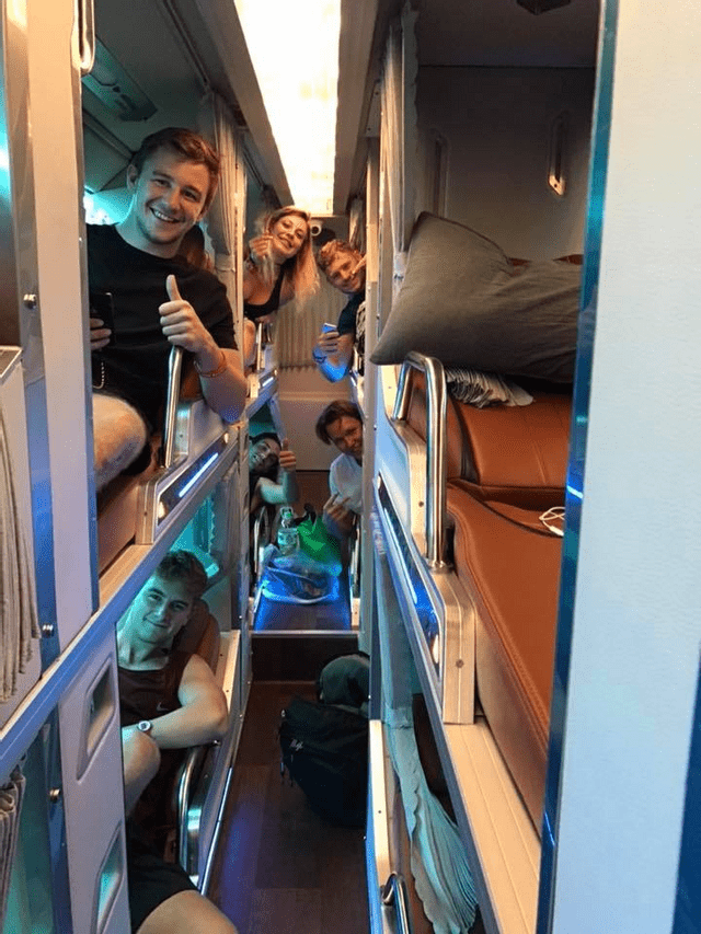Un gruppo WeRoad in viaggio sorride e posa per la fotocamera dalle proprie capsule letto individuali all'interno di un moderno autobus notturno.